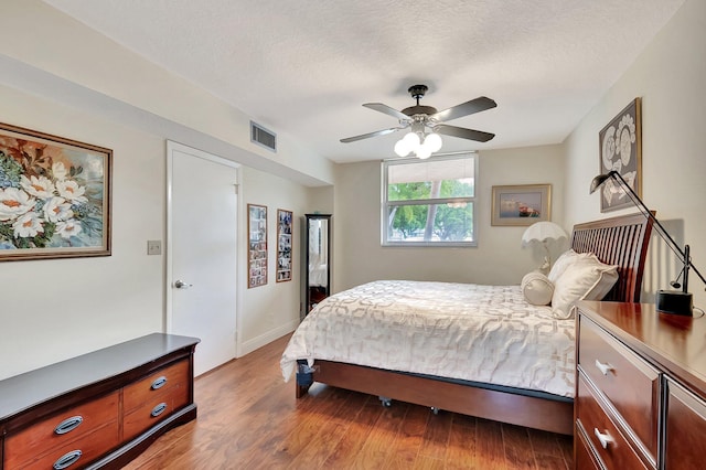 bedroom featuring visible vents, baseboards, ceiling fan, wood finished floors, and a textured ceiling