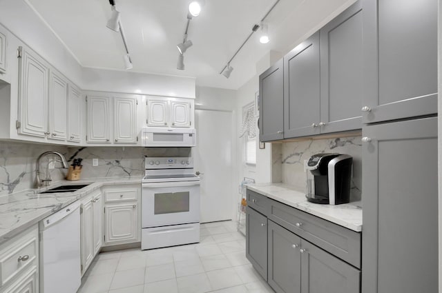 kitchen with gray cabinets, a sink, backsplash, white appliances, and light stone countertops