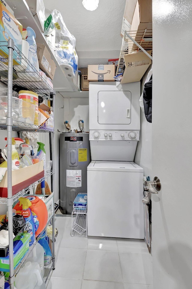 laundry area with tile patterned flooring, stacked washer / dryer, electric water heater, and laundry area