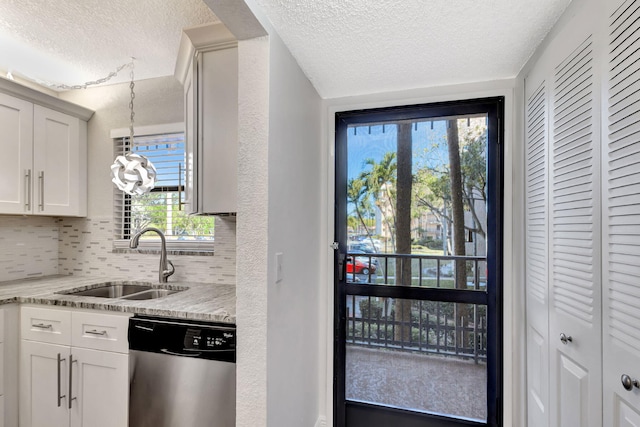 kitchen with a sink, tasteful backsplash, a textured ceiling, white cabinets, and dishwasher