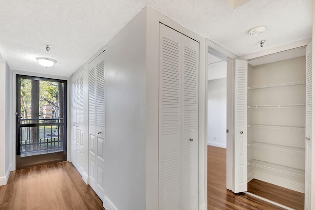 hallway with wood finished floors, baseboards, and a textured ceiling