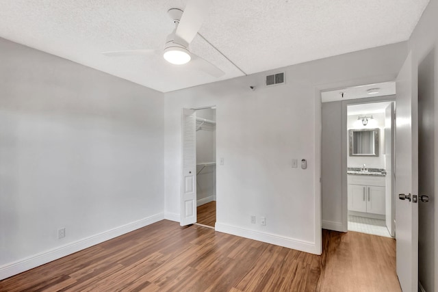 unfurnished bedroom with visible vents, a textured ceiling, baseboards, and wood finished floors