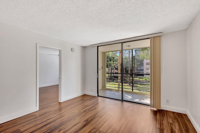 empty room with a textured ceiling, a wall of windows, baseboards, and wood finished floors