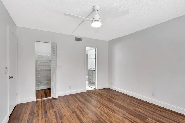 unfurnished bedroom with wood finished floors, visible vents, baseboards, a textured ceiling, and a walk in closet