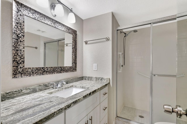 bathroom with vanity, visible vents, a shower stall, a textured ceiling, and a textured wall