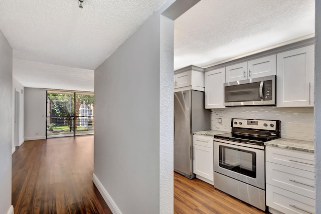 kitchen with tasteful backsplash, baseboards, light stone counters, light wood-style floors, and stainless steel appliances