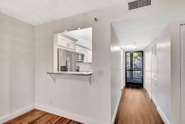 kitchen featuring visible vents, baseboards, appliances with stainless steel finishes, wood finished floors, and white cabinets