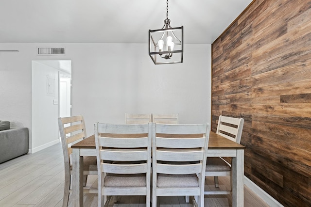 dining area featuring wooden walls, a notable chandelier, visible vents, and light wood finished floors