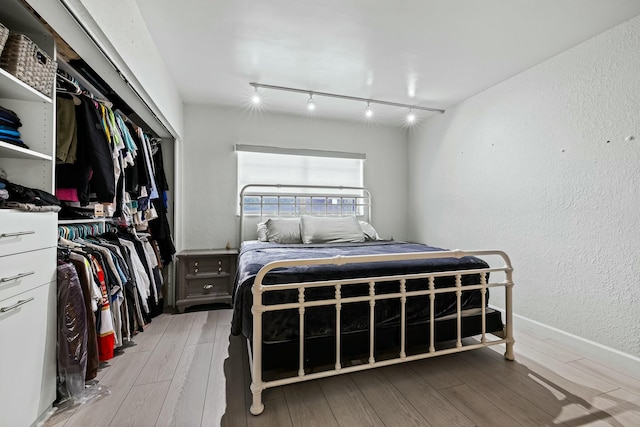 bedroom featuring a closet, track lighting, a textured wall, and wood finished floors