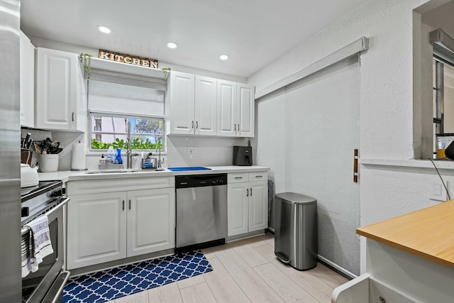 kitchen with light countertops, stainless steel appliances, a textured wall, white cabinetry, and a sink