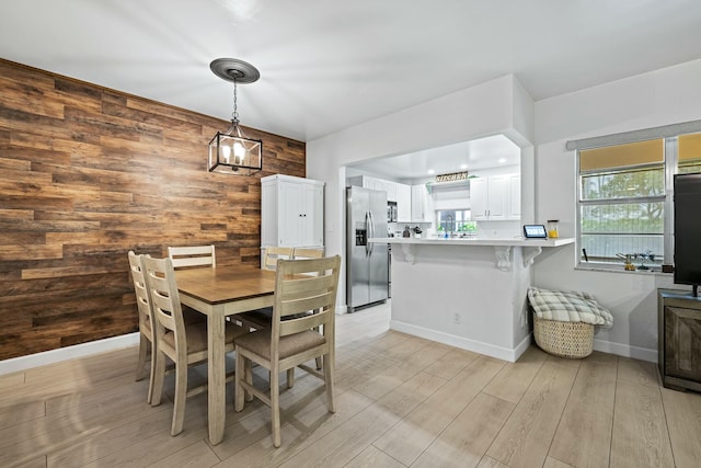 dining area featuring wooden walls, baseboards, and light wood-type flooring