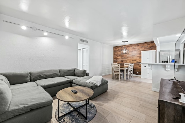 living area with visible vents, an accent wall, baseboards, wood walls, and light wood-style floors