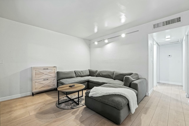 living room with visible vents, rail lighting, light wood-type flooring, and baseboards