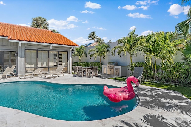 outdoor pool with a patio, area for grilling, and exterior kitchen