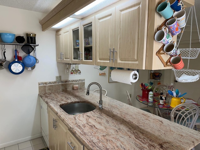 kitchen featuring light stone countertops, baseboards, a sink, tile patterned flooring, and glass insert cabinets