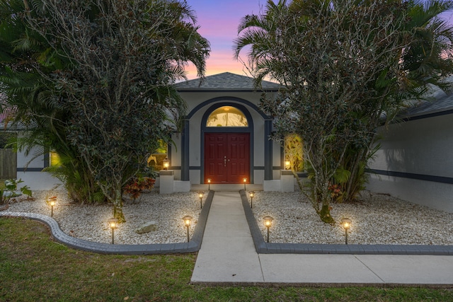 property entrance with stucco siding and a shingled roof