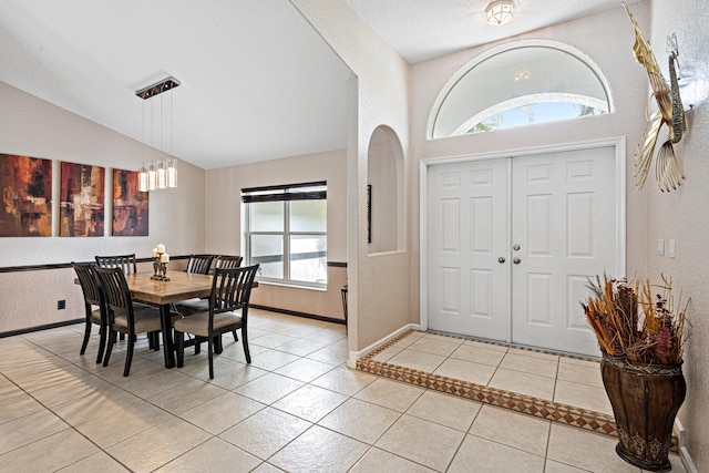entryway with baseboards, lofted ceiling, light tile patterned flooring, and a textured wall