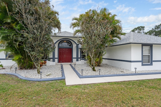 view of front of house featuring stucco siding, a shingled roof, and a front lawn