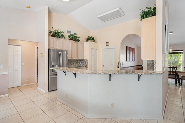 kitchen featuring light tile patterned flooring, a kitchen breakfast bar, stainless steel refrigerator with ice dispenser, and light stone countertops