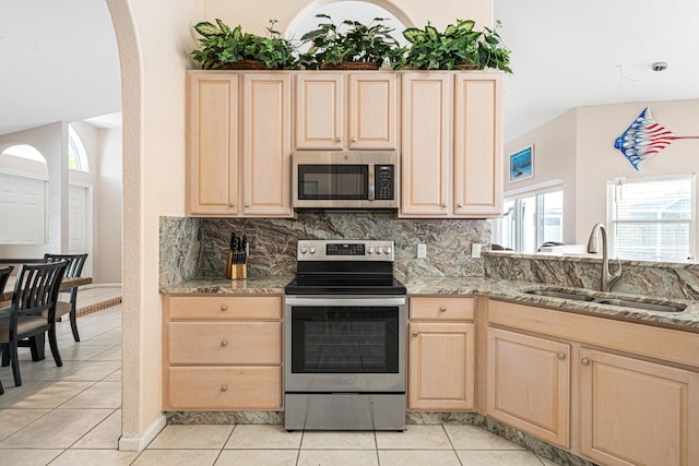 kitchen featuring light brown cabinets, a sink, backsplash, stainless steel appliances, and light tile patterned floors