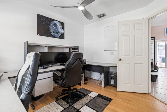 home office with visible vents, light wood-style floors, ceiling fan, and a textured ceiling