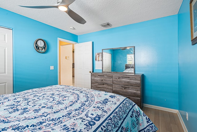 bedroom with visible vents, a ceiling fan, a textured ceiling, wood finished floors, and baseboards