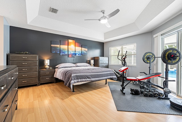 bedroom with a tray ceiling, light wood-style flooring, and visible vents