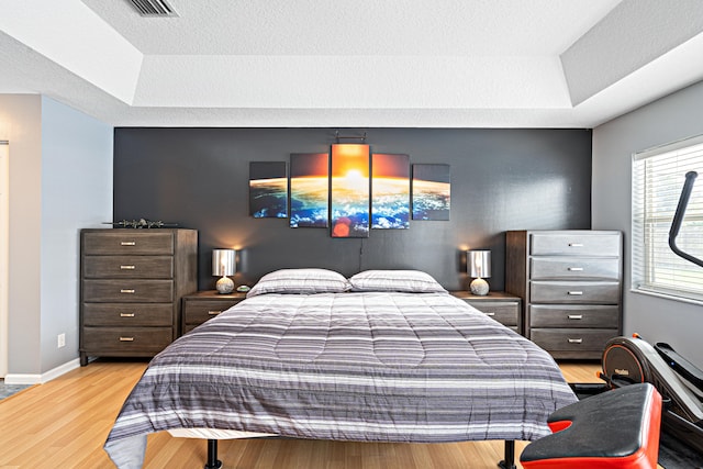 bedroom with baseboards, a raised ceiling, a textured ceiling, and wood finished floors