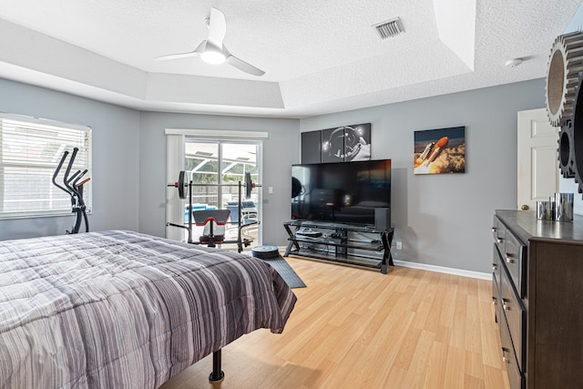 bedroom featuring visible vents, a tray ceiling, light wood-style floors, a textured ceiling, and access to outside