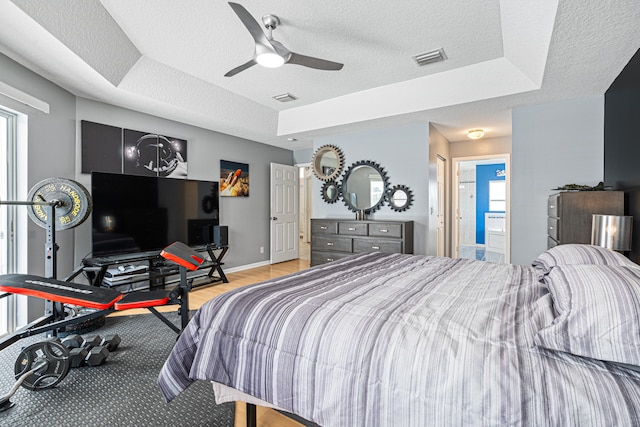 bedroom featuring a tray ceiling, baseboards, a textured ceiling, and visible vents