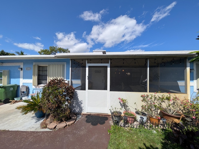 rear view of house with stucco siding and a sunroom