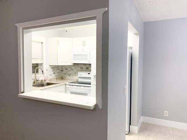 kitchen with a sink, backsplash, white cabinetry, white appliances, and baseboards