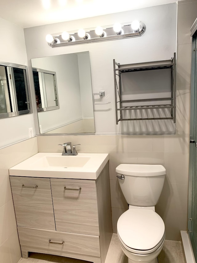 full bathroom featuring a shower with shower door, toilet, tile walls, and vanity