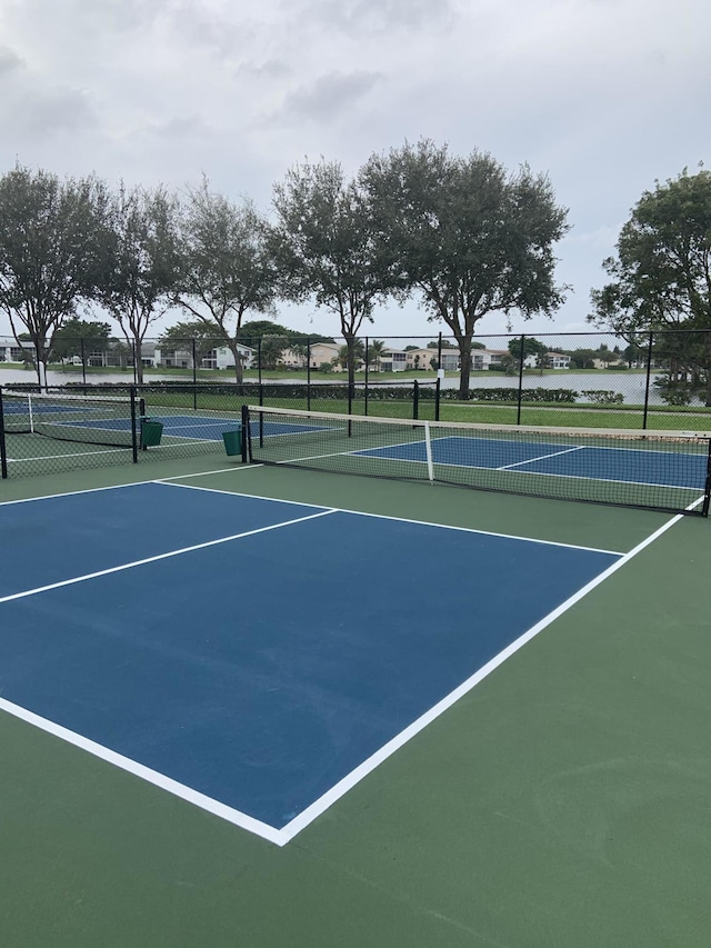 view of tennis court featuring community basketball court, fence, and a water view