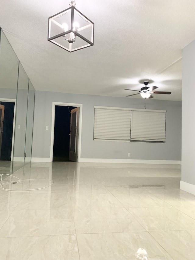 empty room with a textured ceiling, baseboards, marble finish floor, and ceiling fan