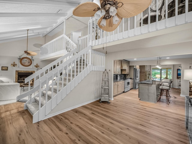 stairs with a fireplace, high vaulted ceiling, ceiling fan, and wood finished floors