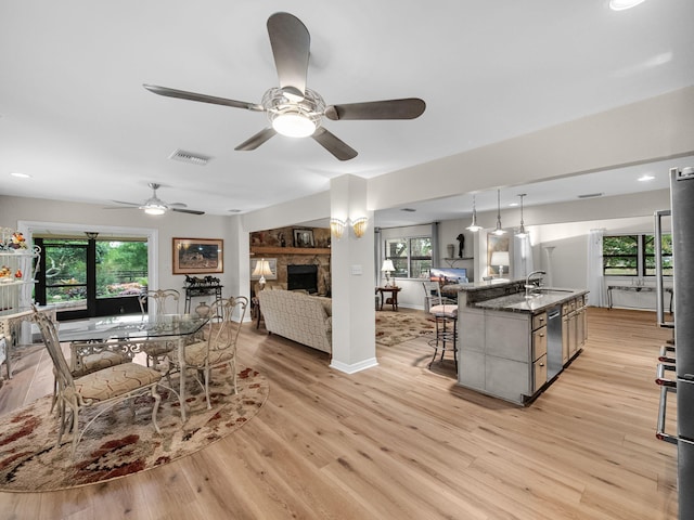 living area featuring a fireplace, a ceiling fan, visible vents, and light wood finished floors