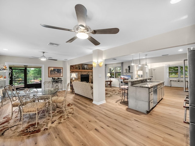 living room with visible vents, light wood-style flooring, a stone fireplace, baseboards, and ceiling fan