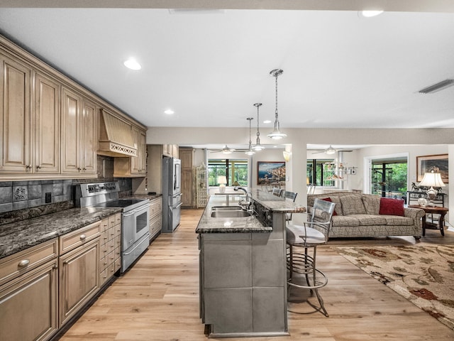 kitchen featuring a breakfast bar, custom exhaust hood, a sink, ceiling fan, and stainless steel appliances