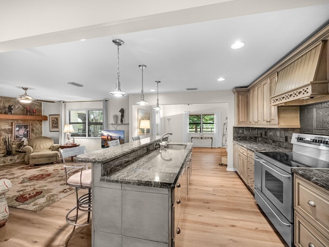 kitchen featuring a sink, electric stove, a kitchen bar, tasteful backsplash, and light wood-type flooring