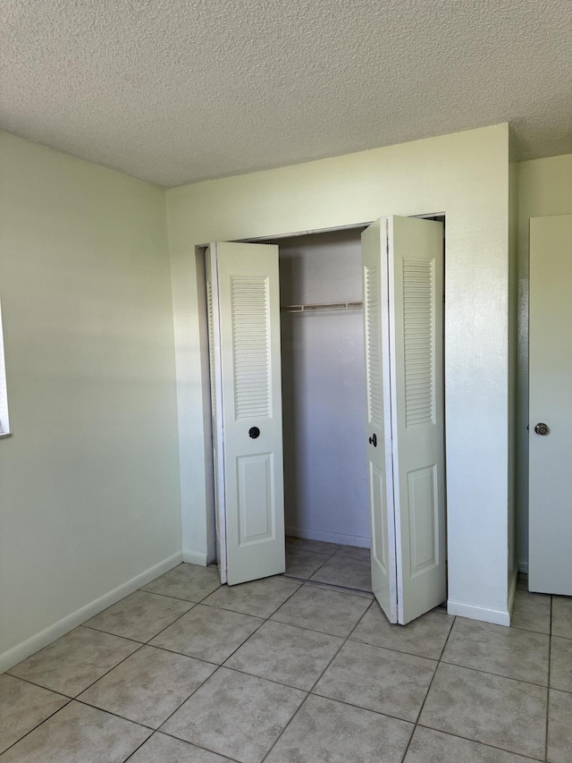 unfurnished bedroom featuring light tile patterned flooring, a textured ceiling, and baseboards