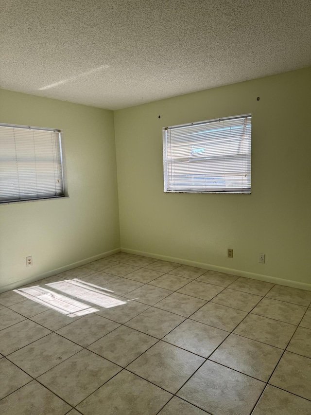 spare room with light tile patterned floors, baseboards, and a textured ceiling