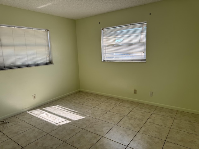 unfurnished room featuring light tile patterned floors, a textured ceiling, and baseboards