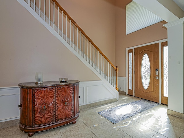 entrance foyer with tile patterned flooring, stairway, wainscoting, and a decorative wall