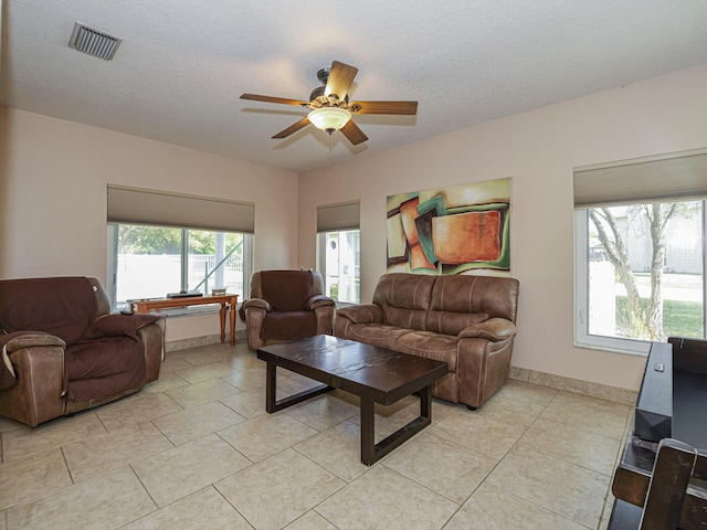 living room with light tile patterned flooring, visible vents, a textured ceiling, and ceiling fan