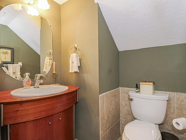 bathroom featuring vanity, vaulted ceiling, a textured ceiling, tile walls, and toilet