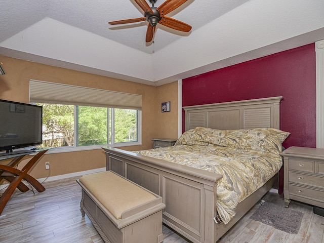 bedroom with light wood-style flooring, baseboards, a raised ceiling, and a ceiling fan