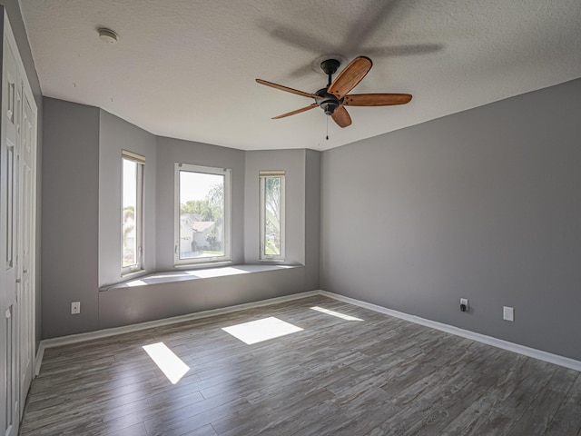 spare room with a ceiling fan, wood finished floors, baseboards, and a textured ceiling