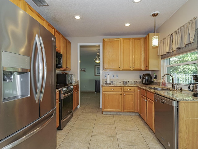 kitchen with light stone counters, light tile patterned floors, a sink, stainless steel appliances, and decorative light fixtures