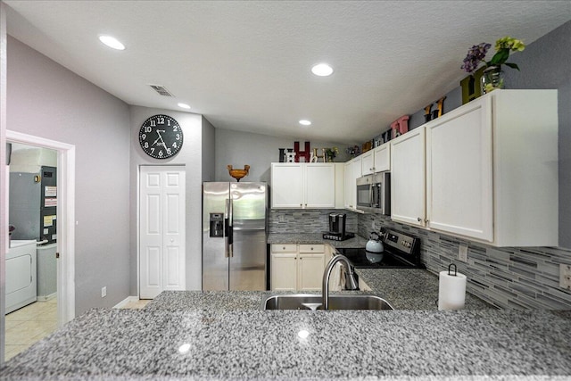 kitchen with washer / clothes dryer, stone countertops, a sink, appliances with stainless steel finishes, and backsplash